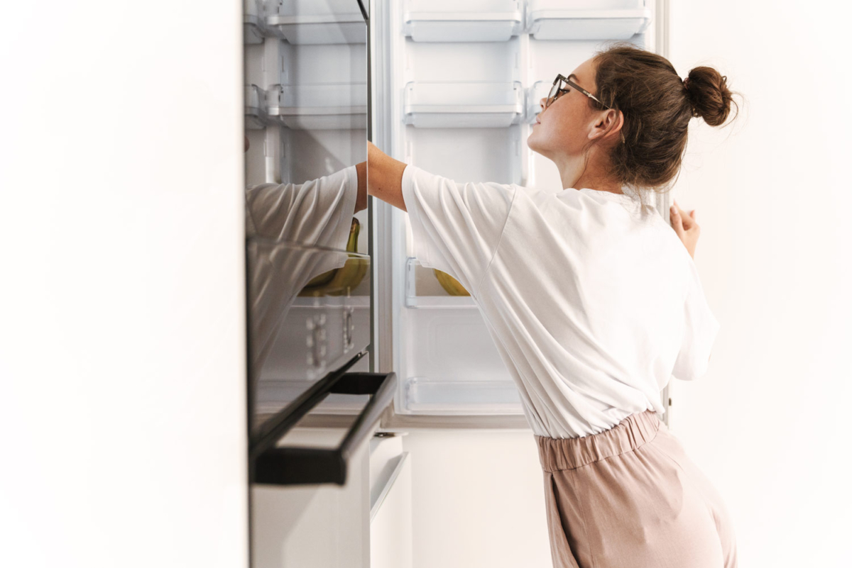 Junge Frau wischt einen Kühlschrank aus.